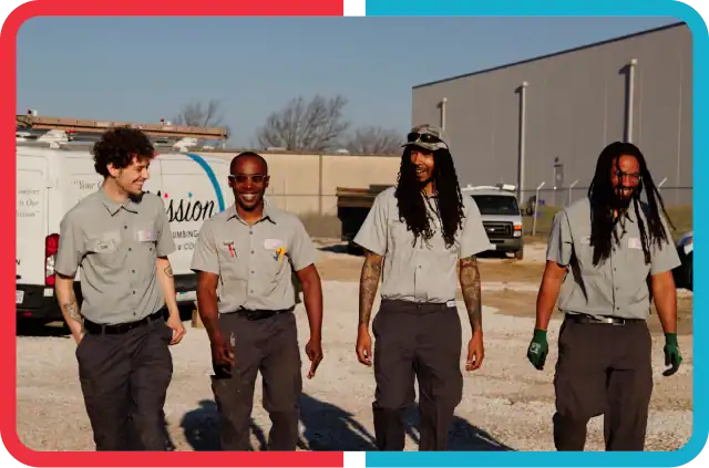 Four men in matching gray uniforms walk outside on gravel near a white van and a large building, smiling as they talk together.